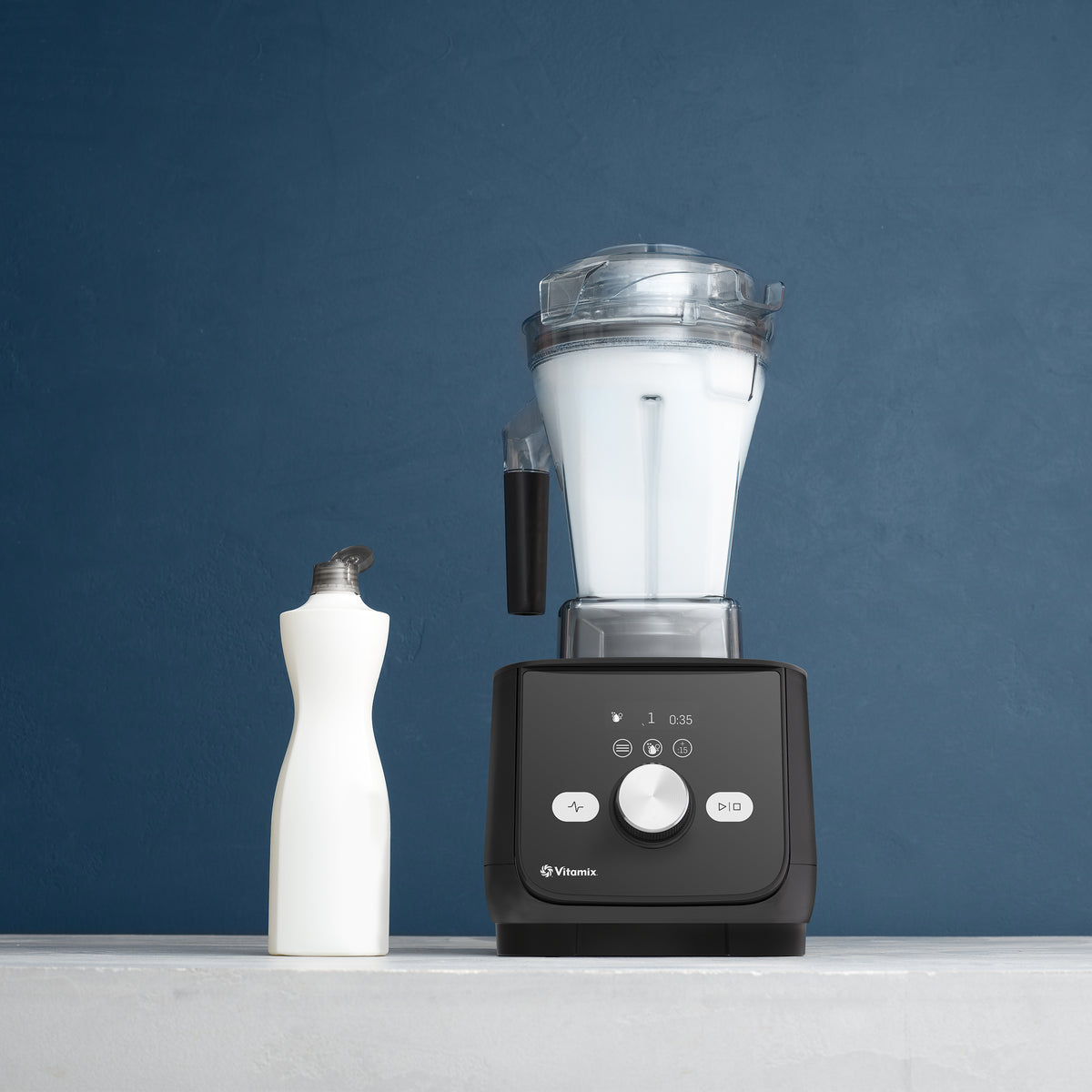 Vitamix Ascent X5 Blender in Shadow Black running its self-cleaning program, with a bottle of dish soap beside it