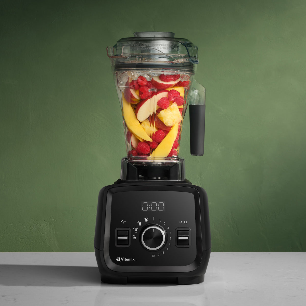 Vitamix VX3 Blender in Black filled with fresh fruit on a green background