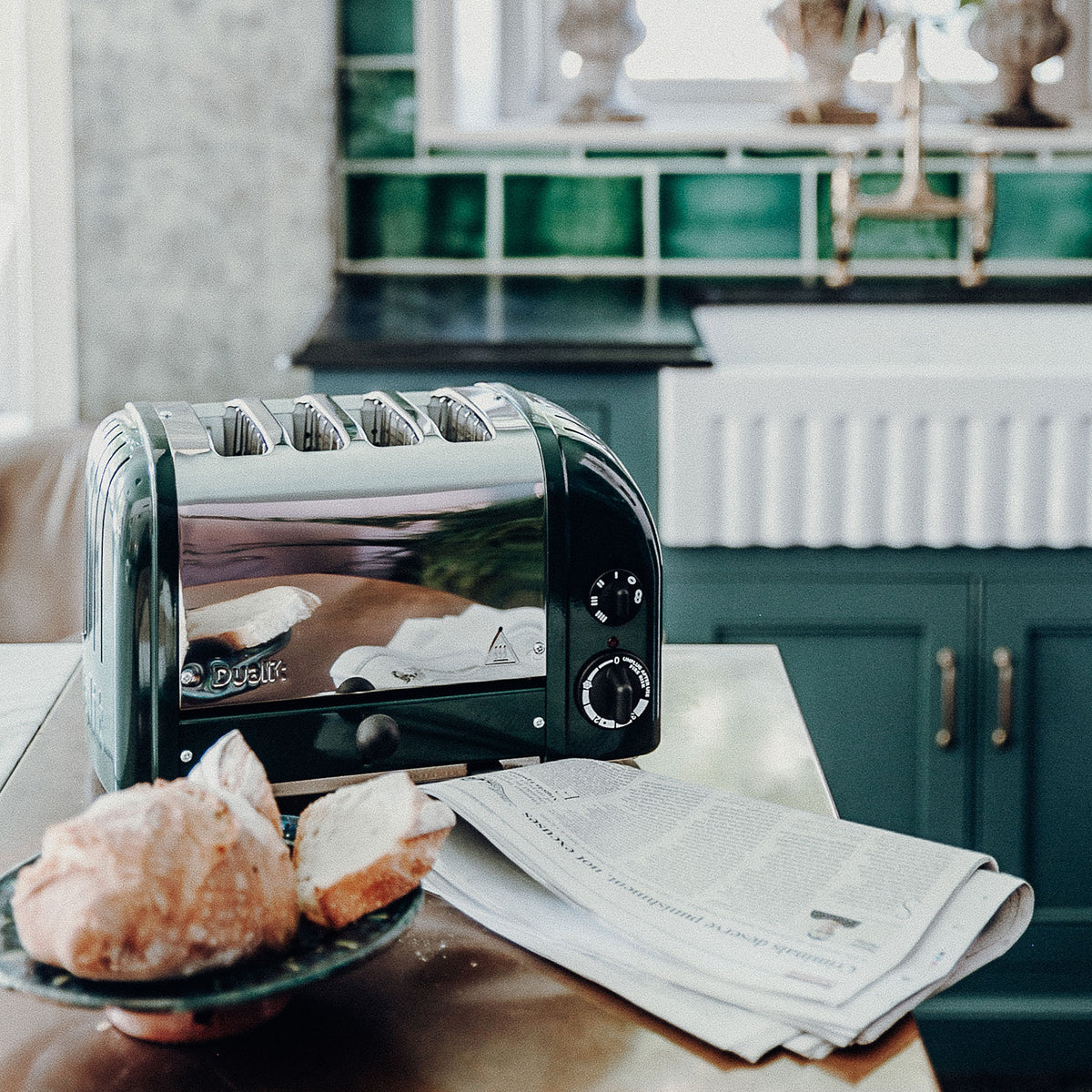 Dualit Classic 4-slice toaster in evergreen with crusty bread and a newspaper in a green tiled kitchen