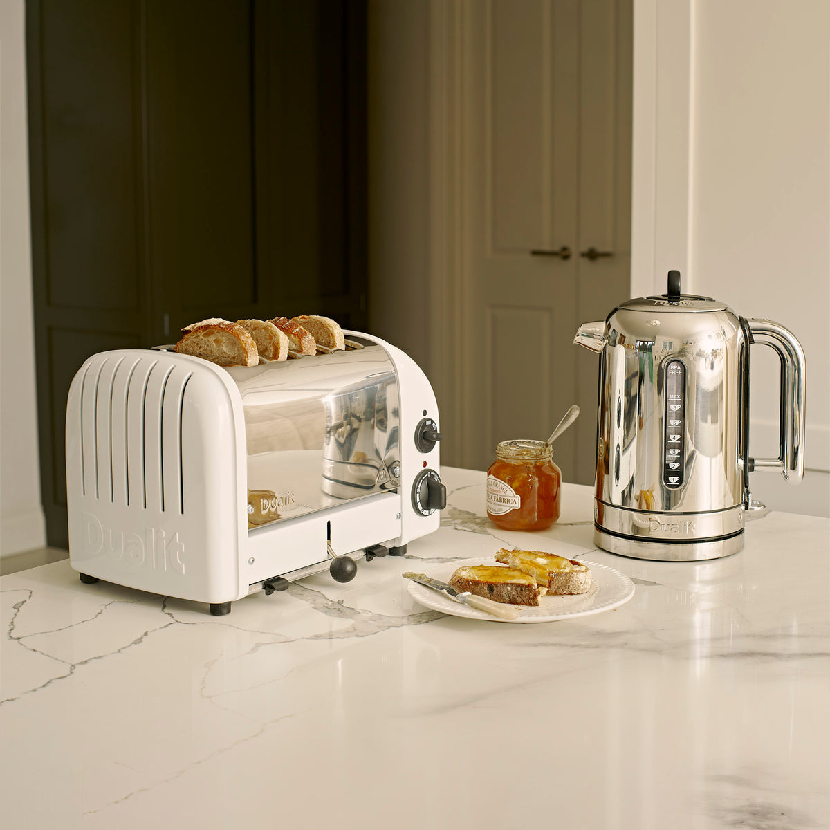 Dualit Classic 4-slice toaster in white with toast beside a Dualit Classic kettle on a marble counter, with marmalade on toast