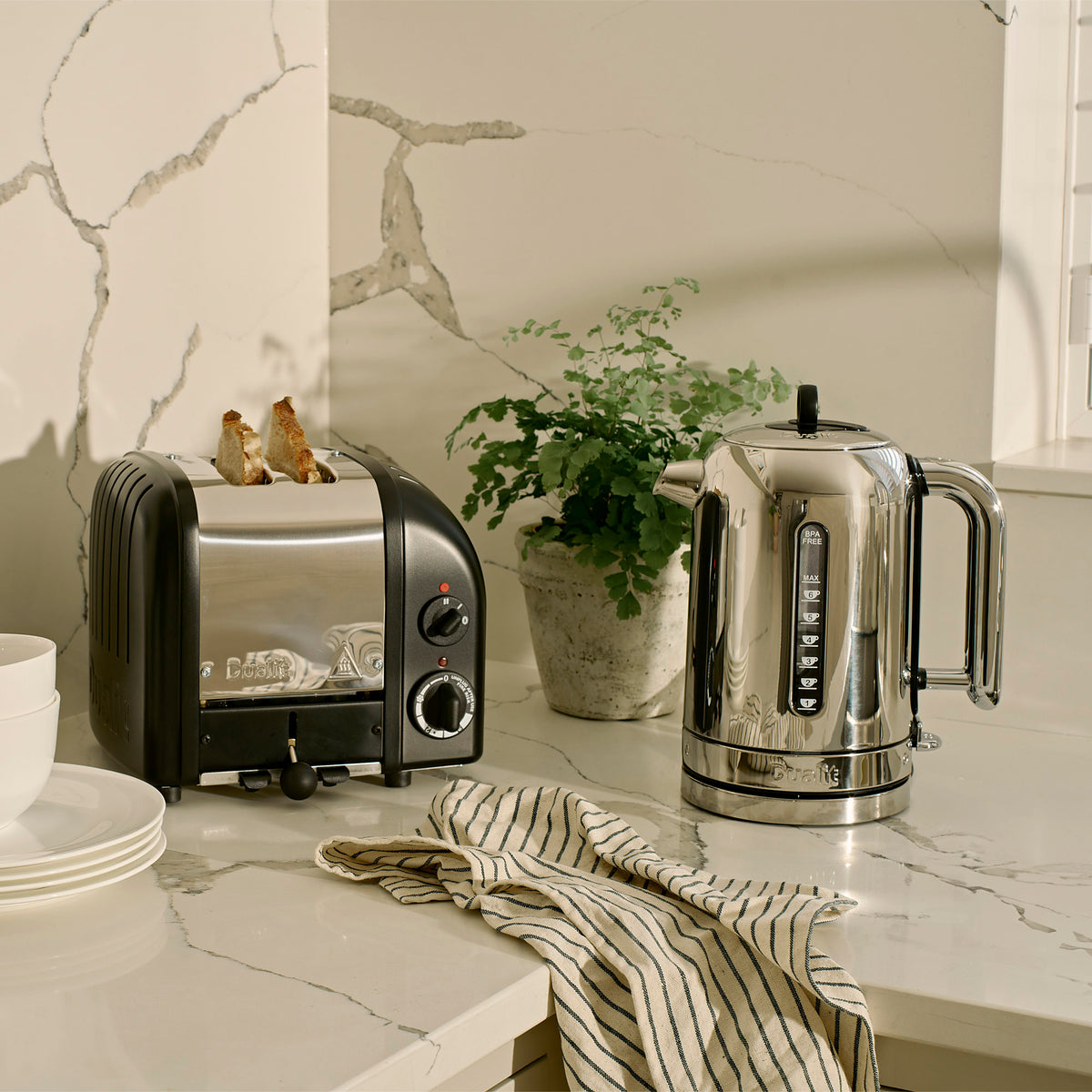 Dualit Classic 2-slice toaster in matt black beside a Dualit Classic kettle and a potted plant on a marble counter