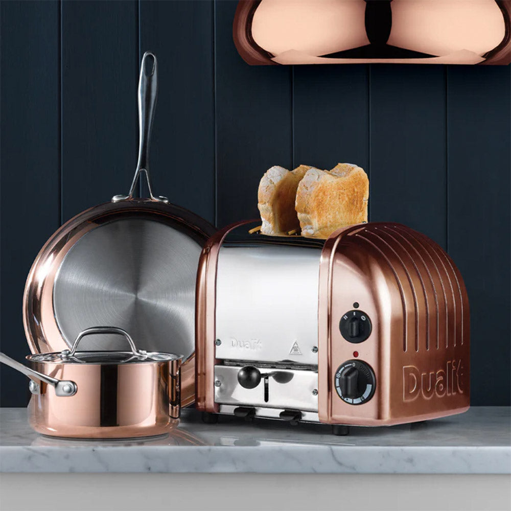 Dualit Classic 2-slice toaster in copper with toast beside copper pans against a navy panelled wall