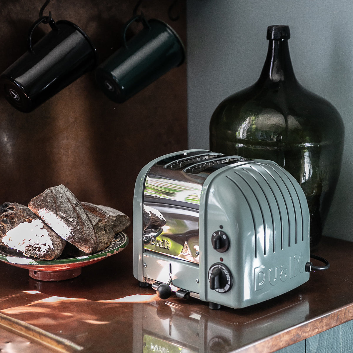 Dualit Classic 2-slice toaster in eucalyptus with crusty bread and a green glass bottle on a copper counter