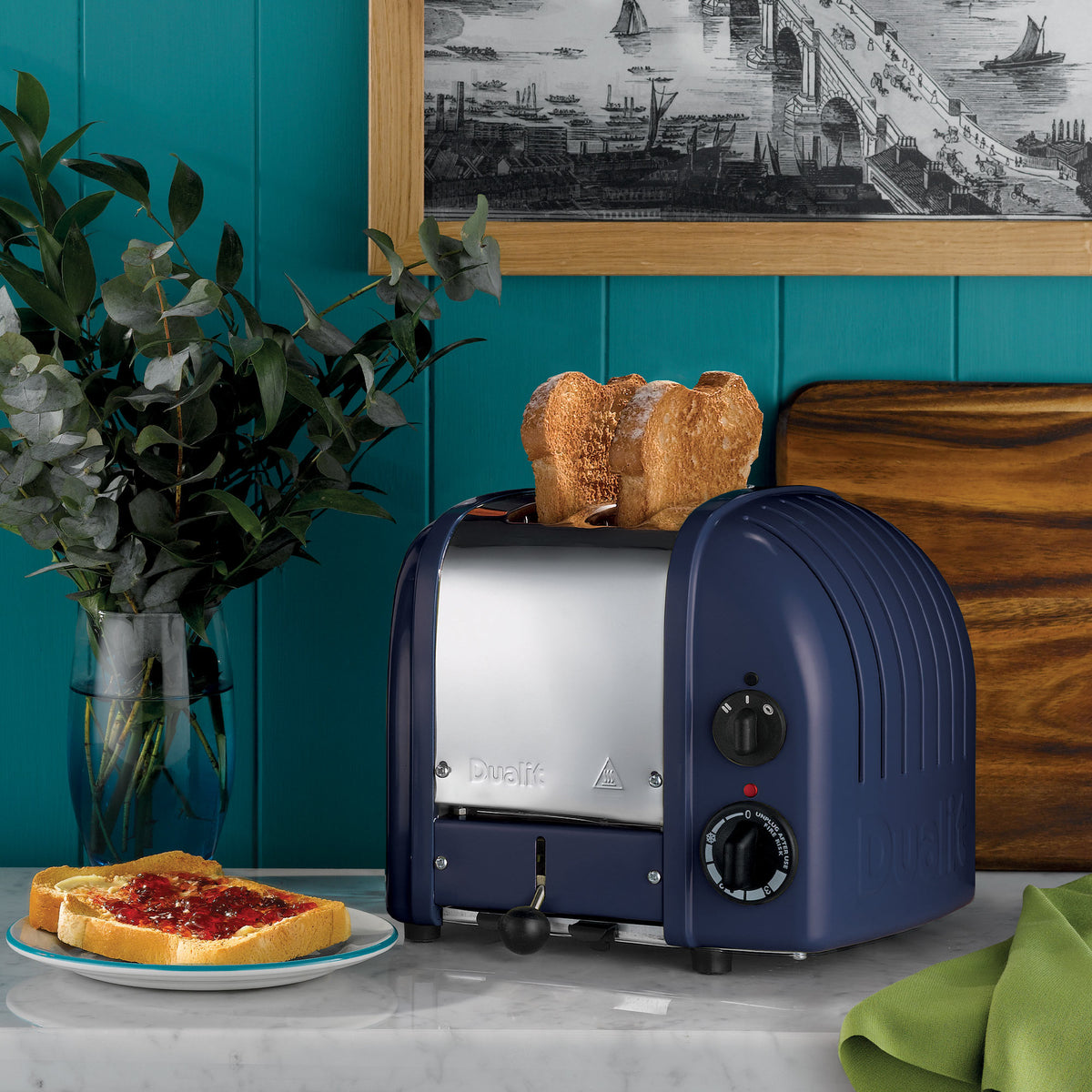 Dualit Classic 2-slice toaster in lavender blue with toast on a marble counter against a teal panelled wall, with jam on toast and eucalyptus