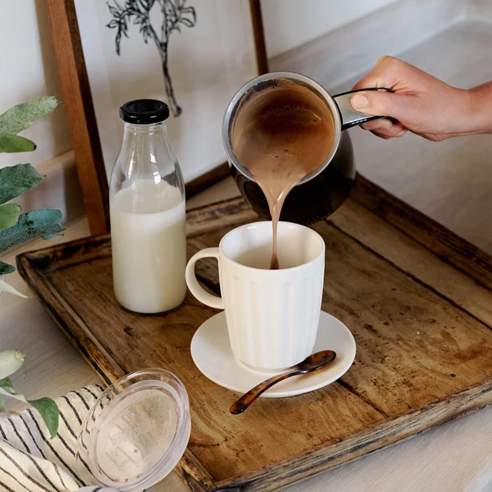 Pouring hot chocolate from the Dualit jug into a white mug on a wooden tray