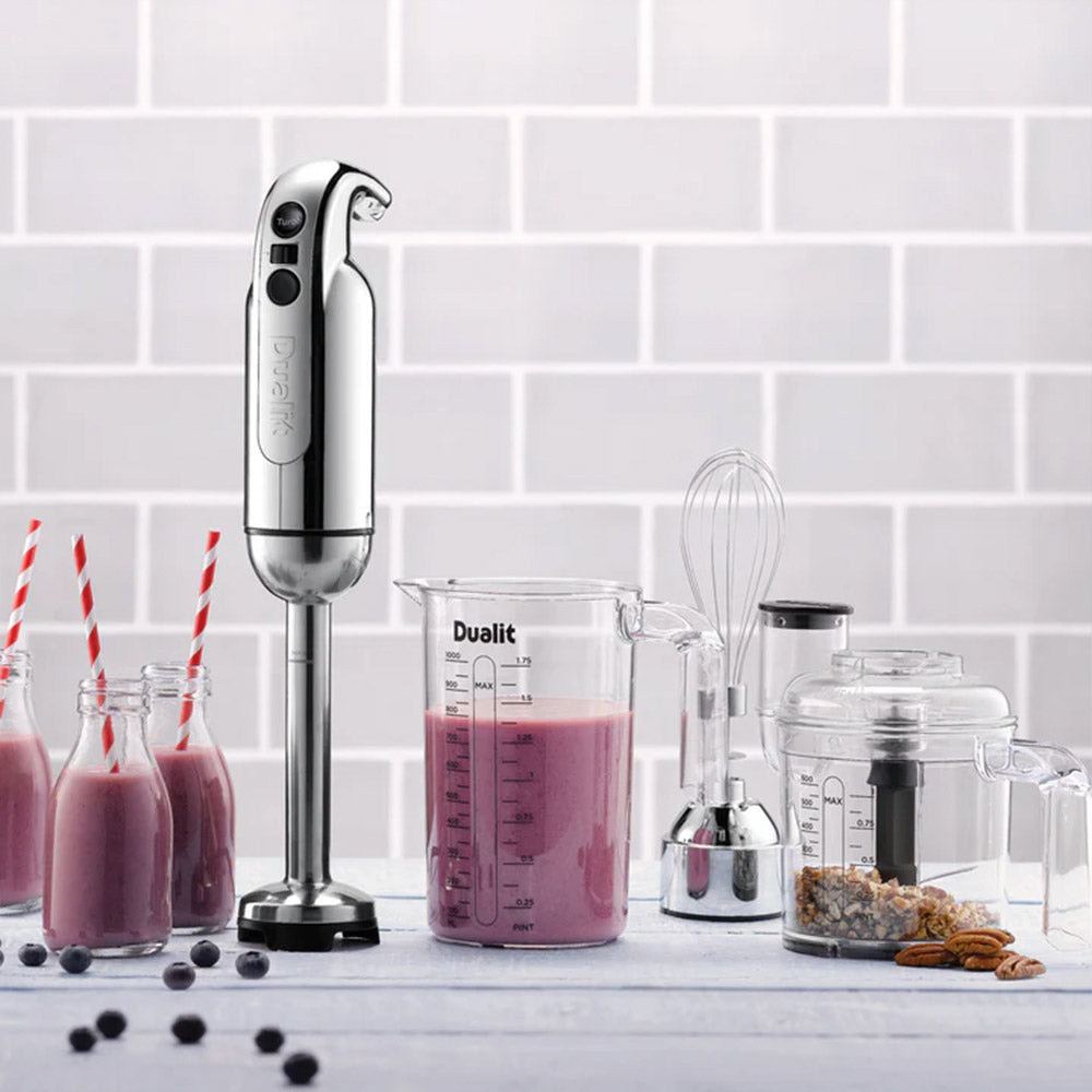 Dualit hand blender with a berry smoothie in the jug, milk bottles and the chopper against grey tiles