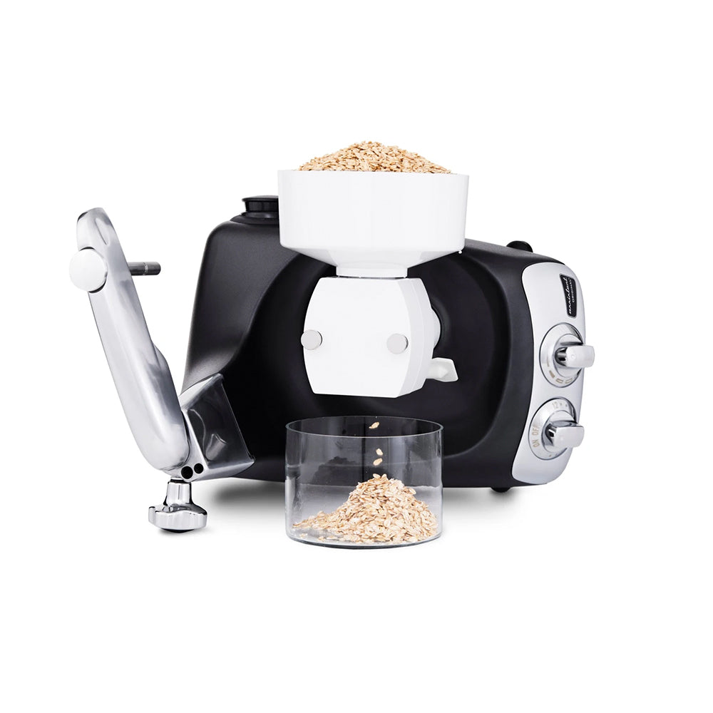 Ankarsrum Flake Mill on a black Ankarsrum Assistent Original laid on its back, rolling oat flakes into a glass bowl