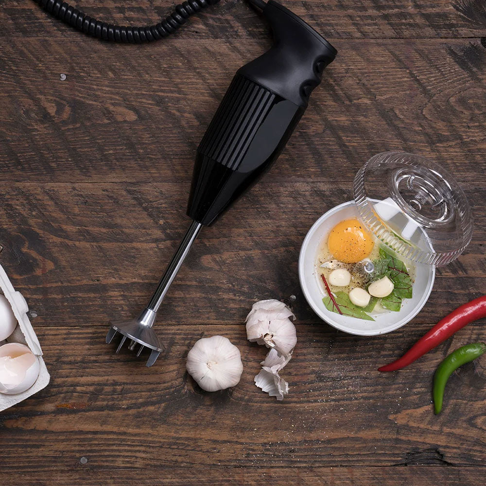 Black bamix hand blender on a dark wooden table beside garlic, chillies and an egg in a small bowl