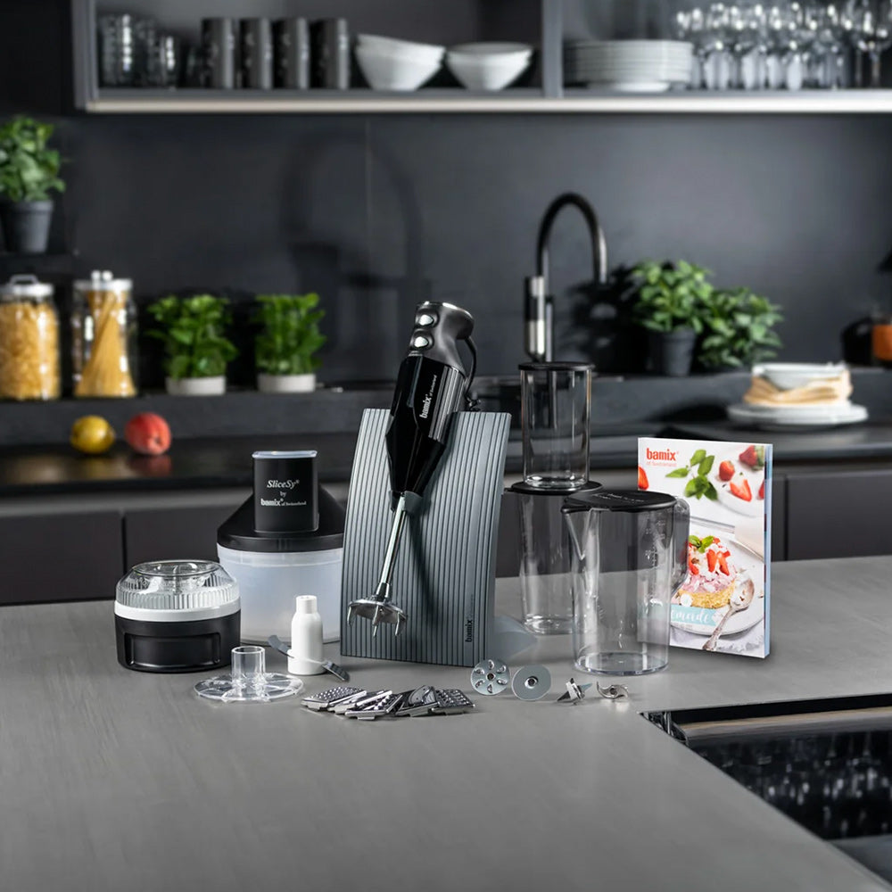 bamix BAKING set on a grey kitchen counter: hand blender in its stand, Processor, SliceSy, beakers and recipe book