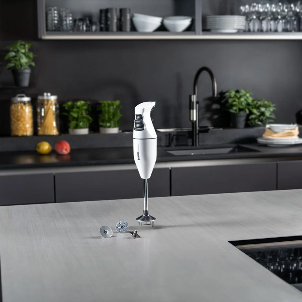 bamix Classic in white standing on a grey kitchen counter with its three attachments