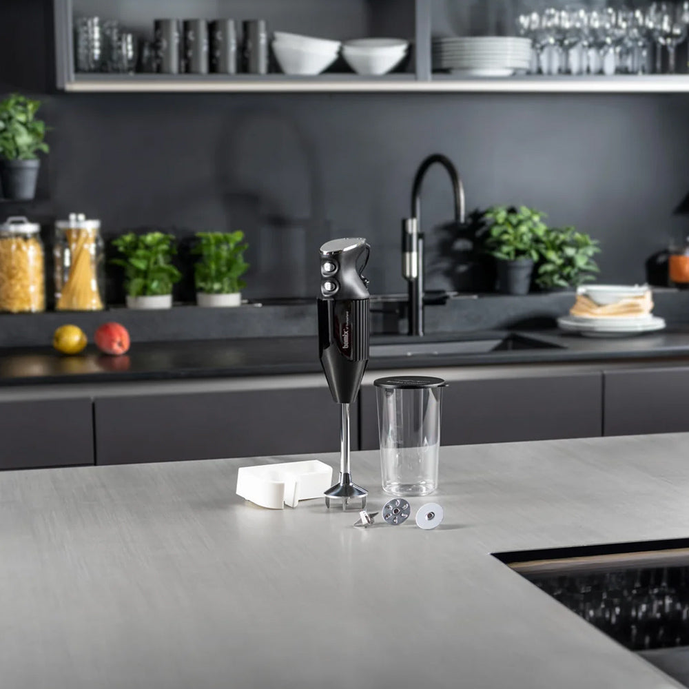 bamix Mono in black on a grey kitchen counter with its beaker, wall holder and attachments