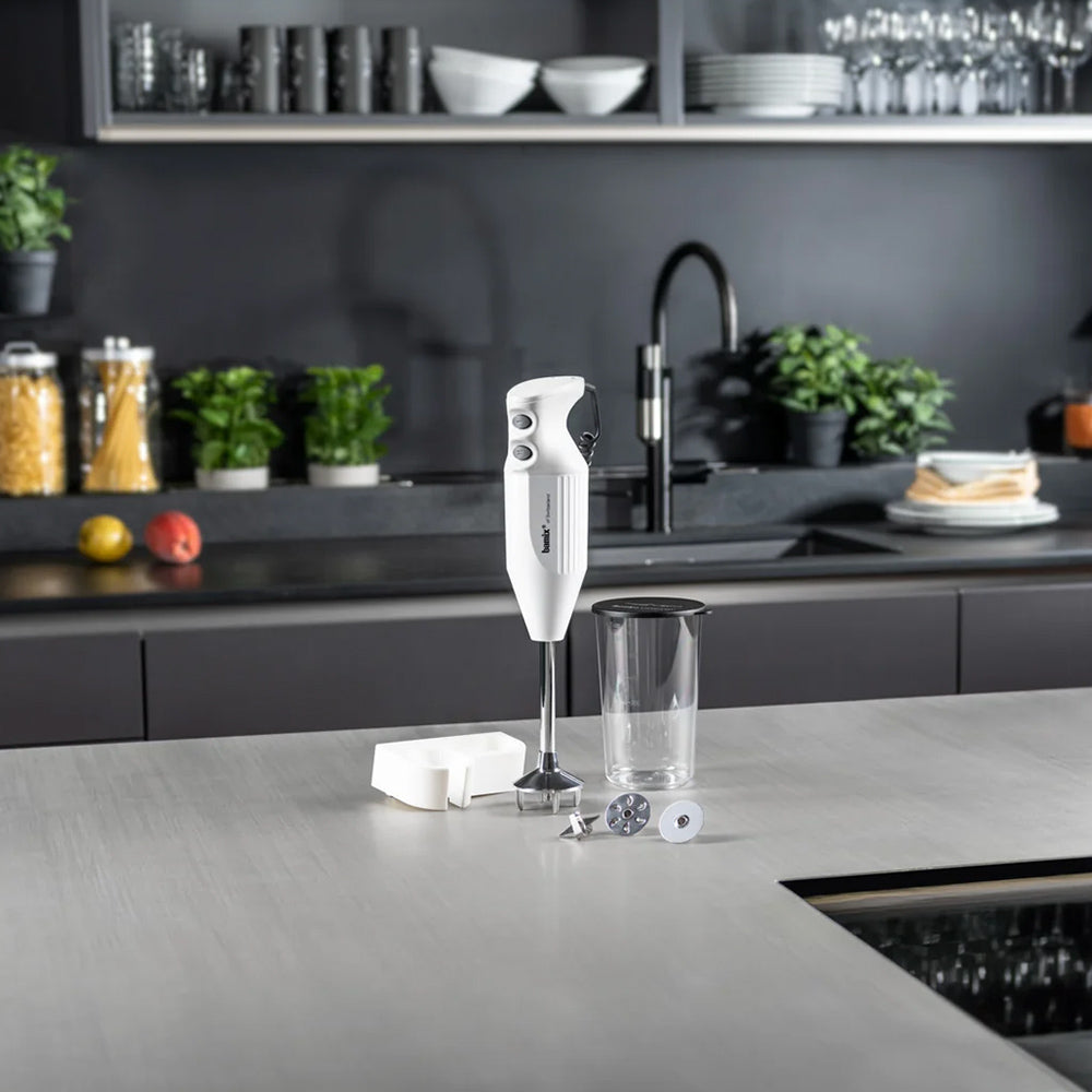 bamix Mono in white on a grey kitchen counter with its beaker, wall holder and attachments