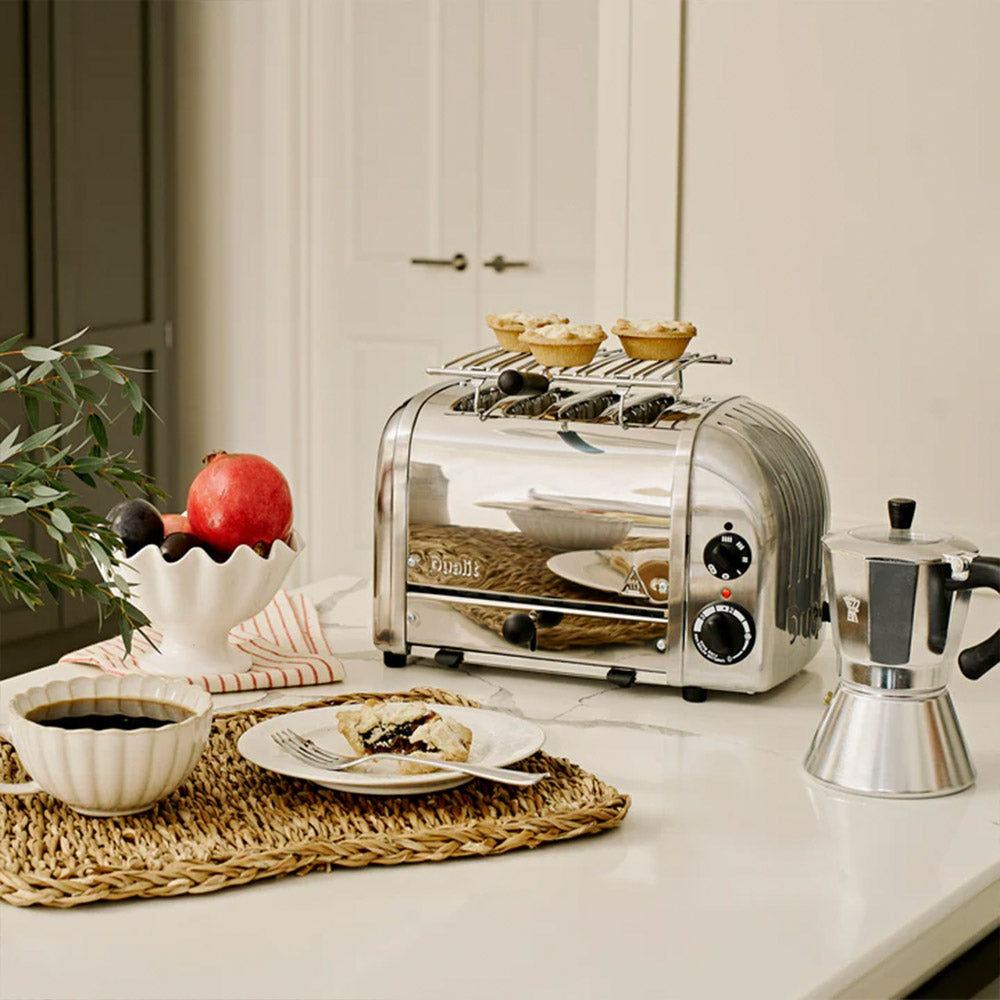Dualit warming rack on a polished Classic 4-slice toaster with pastries, a pomegranate and a moka pot