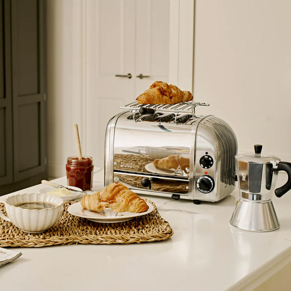 Dualit warming rack on a polished Classic 4-slice toaster with a croissant, jam and a moka pot