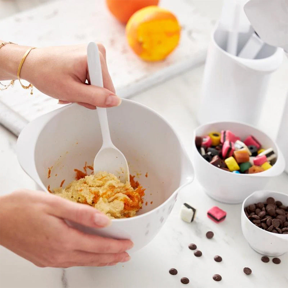 Batter stirred in a white Rosti Margrethe mixing bowl beside small bowls of sweets and chocolate chips