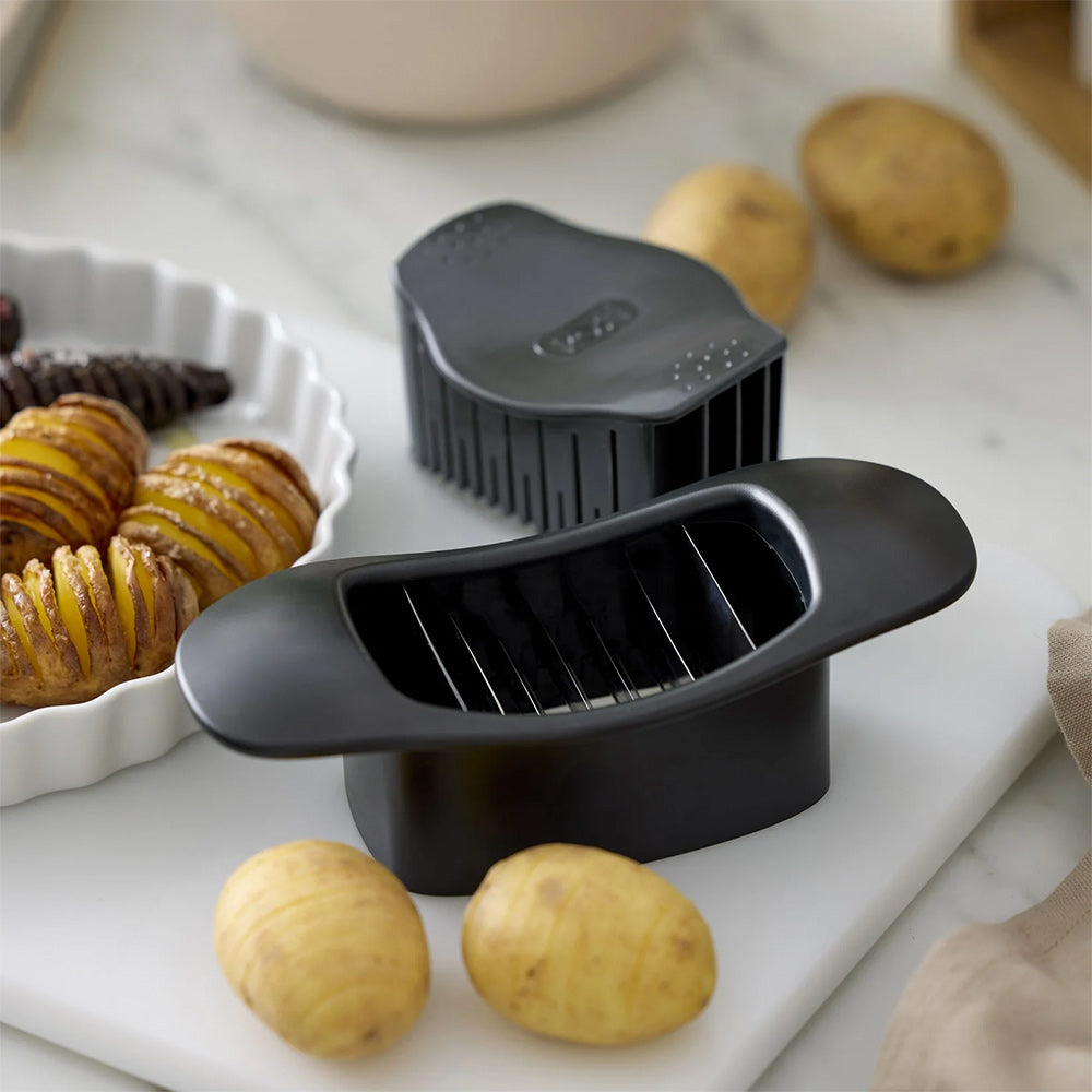 Rosti Hasselback cutter in Black beside potatoes and a dish of baked Hasselback potatoes