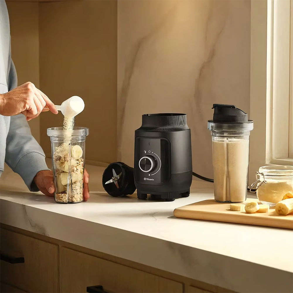 Adding ingredients to a cup beside a Vitamix Nano Personal Blender in Black