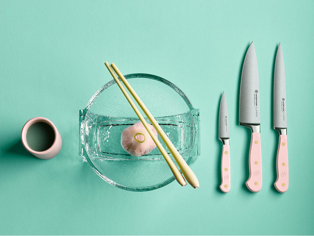 WÜSTHOF CLASSIC knives in Pink Himalayan Salt on a mint background beside a glass bowl, chopsticks and garlic