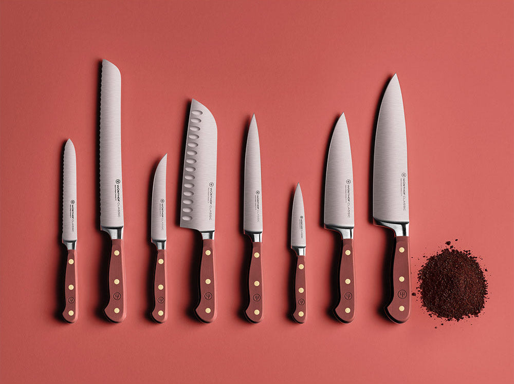 WÜSTHOF CLASSIC knives in Tasty Sumac laid out in a row on a red background beside a heap of ground spice