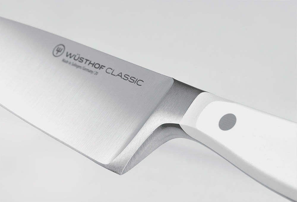 Close-up of the bolster where the blade of a WÜSTHOF CLASSIC knife meets the white handle