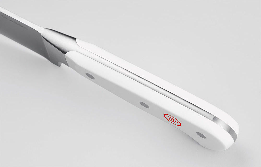 Close-up of the white handle of a WÜSTHOF CLASSIC knife from the spine side, showing the tang and red trident logo