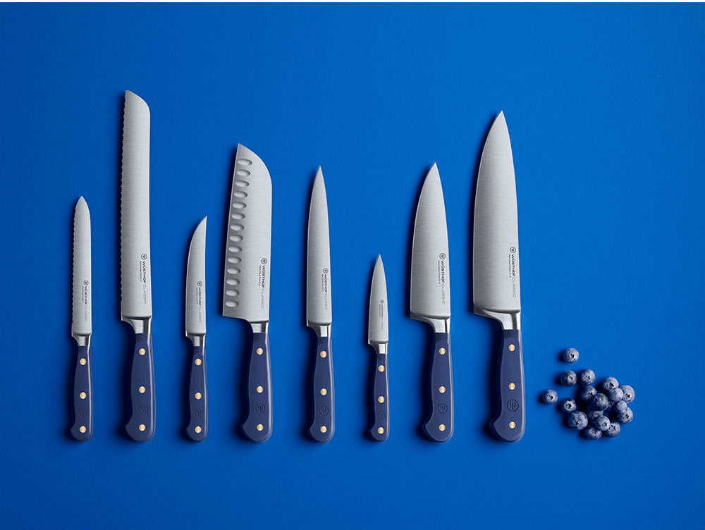WÜSTHOF CLASSIC knives in Wild Blueberry laid out in a row on a blue background beside blueberries
