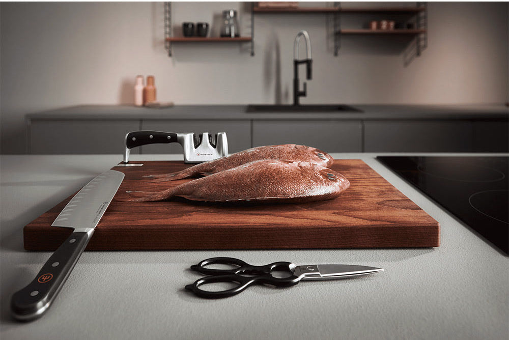 WÜSTHOF CLASSIC IKON 2-Stage Hand-Held Sharpener behind a board with fish, a knife and kitchen shears