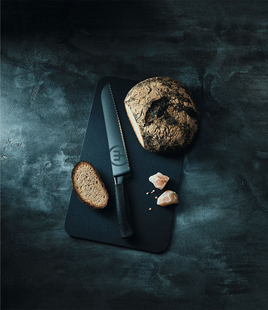 WÜSTHOF PERFORMER 9" Double-Serrated Bread Knife on a dark board with a round loaf and a slice of bread