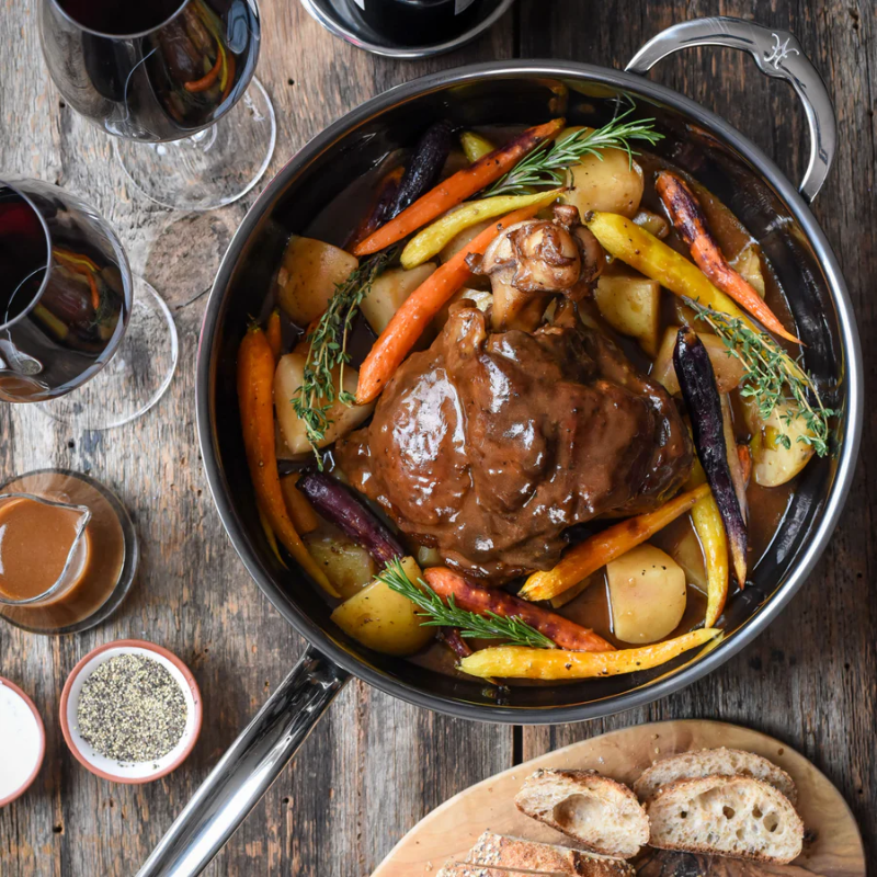 Hestan NanoBond pan of braised lamb shank with roasted carrots and potatoes on a wooden table with red wine