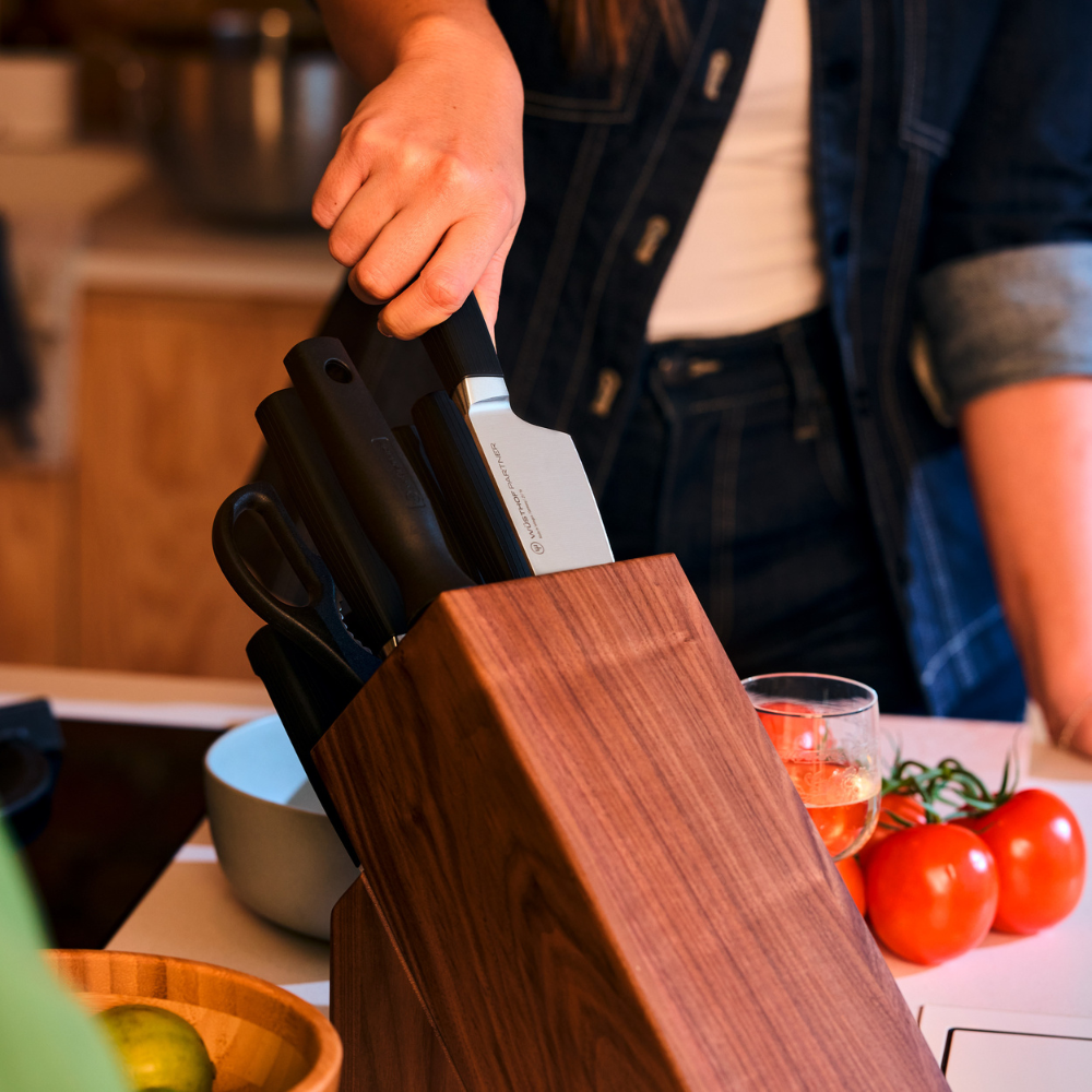 Hand taking a WÜSTHOF PARTNER knife from the wooden block on a kitchen counter, beside tomatoes