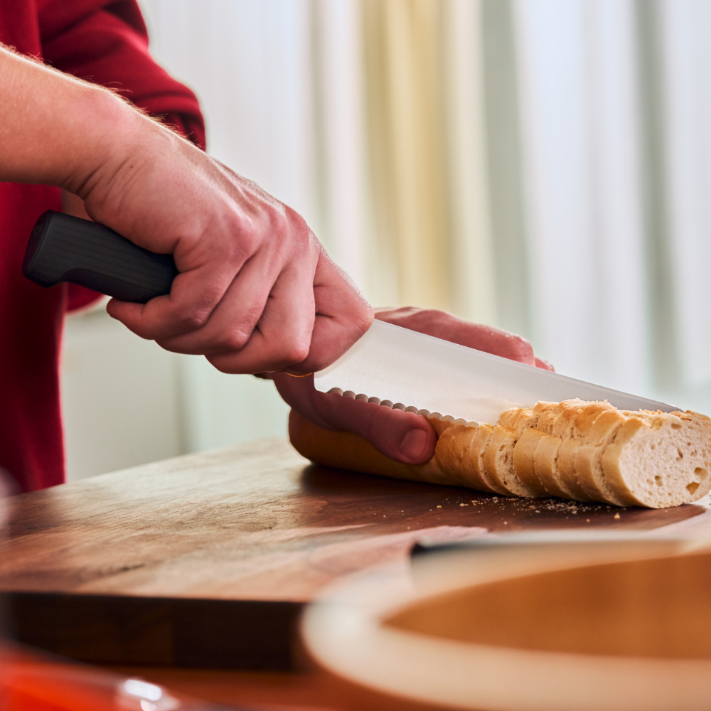 Hands slicing a baguette with the WÜSTHOF PARTNER 8" Bread Knife on a wooden board
