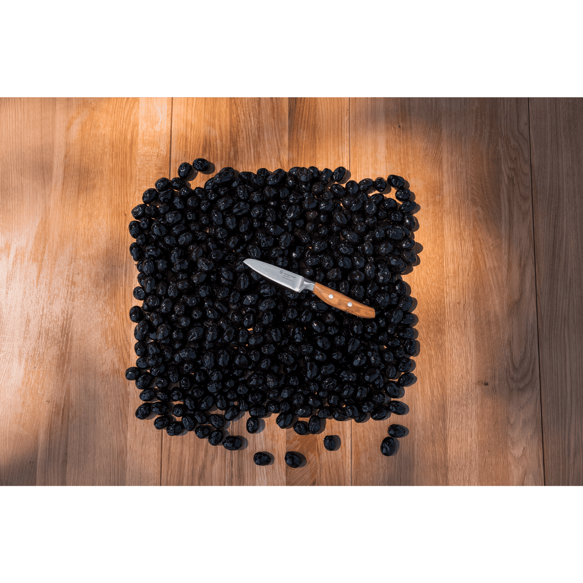 WÜSTHOF AMICI 3.5" Paring Knife on a heap of black olives on a wooden table