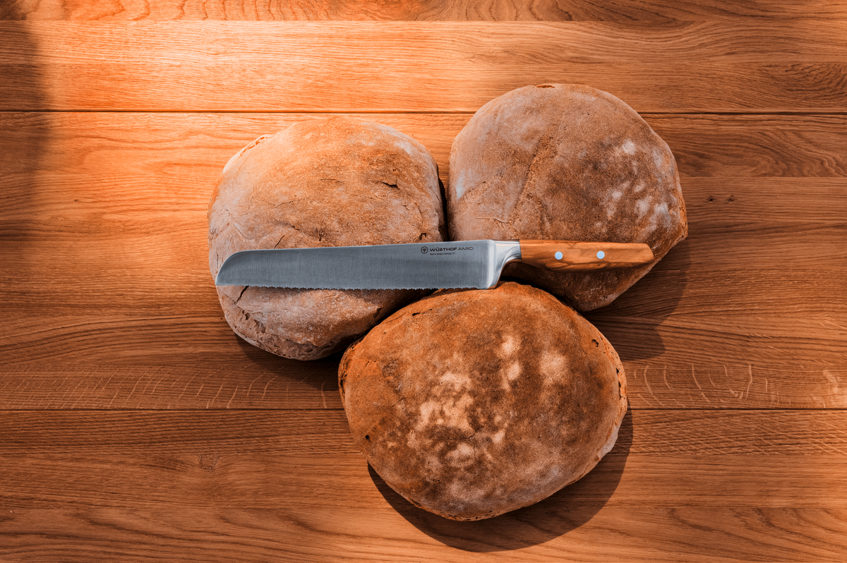 WÜSTHOF AMICI 9" Double-Serrated Bread Knife on round crusty loaves on a wooden table, seen from above