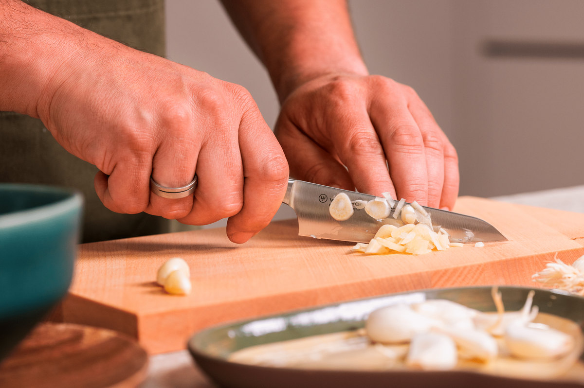 Hands slicing garlic with the WÜSTHOF CLASSIC 4.5" Asian Utility Knife on a wooden board