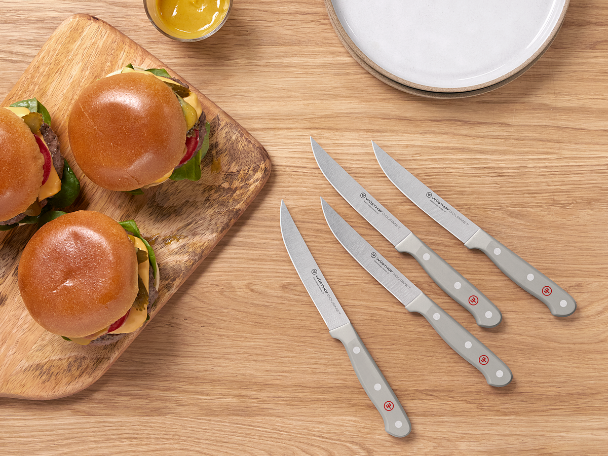WÜSTHOF GOURMET steak knives in grey on a wooden table beside burgers on a board