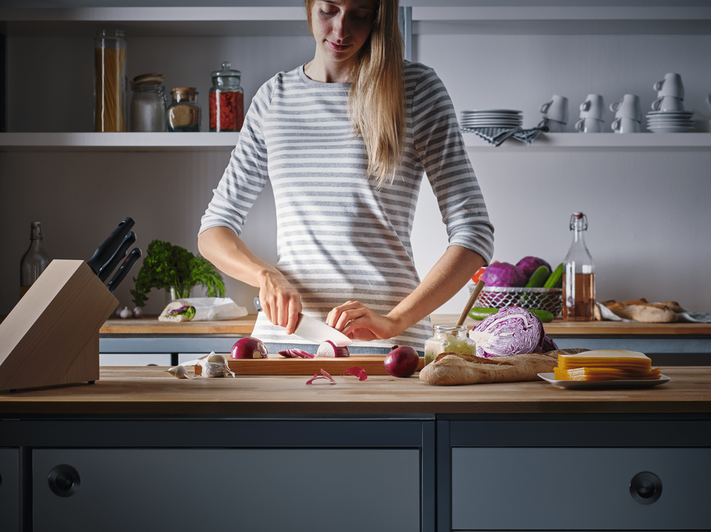 Woman chopping vegetables at a kitchen counter with a WÜSTHOF GOURMET knife, beside a knife block