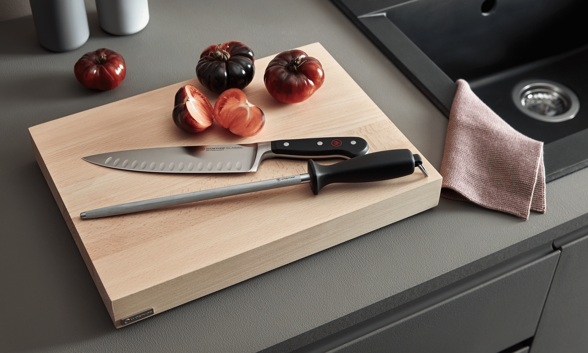 WÜSTHOF 10" Honing Steel with Loop and a chef's knife on a wooden board beside tomatoes and a linen cloth