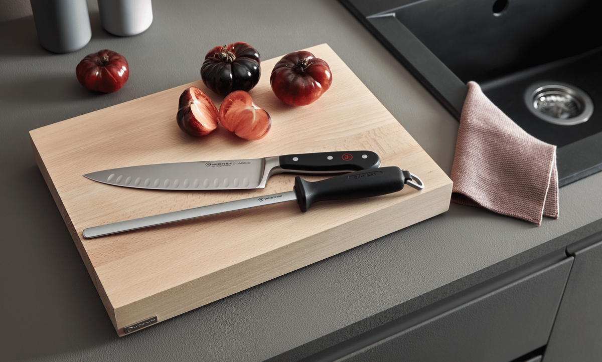 WÜSTHOF 10" Wide Diamond Sharpening Steel and a chef's knife on a wooden board beside tomatoes and a linen cloth